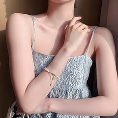 Close-up of a woman wearing a delicate white freshwater pearl and green jade adjustable bracelet paired with a light blue textured sleeveless dress, showcasing elegant jewelry for women.