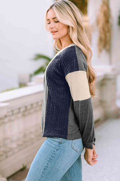 Woman wearing a multicolor color block polyester sweater with navy, cream, and gray panels, paired with light blue jeans, standing outdoors near a stone railing.