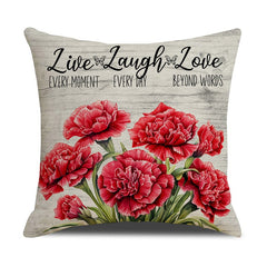 Decorative throw pillow with vibrant red carnations and inspirational text "Live Every Moment Laugh Every Day Love Beyond Words" on a light textured background.