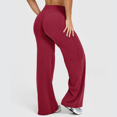 Woman wearing high-waisted, wide straight leg yoga pants in deep red, paired with athletic shoes, shown from the back on a plain light background.