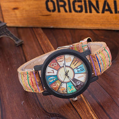 Close-up of a vintage-inspired women's wristwatch with a multicolor dial featuring unique number designs and a retro leather strap on a wooden surface.