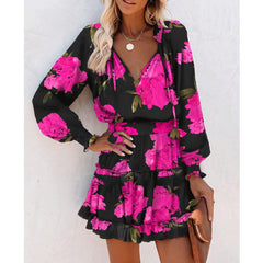 Woman wearing a stylish black dress with bright pink floral print, featuring long puff sleeves, a fitted waist, and a tiered skirt, accessorized with gold jewelry and a brown clutch.