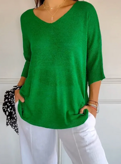 Woman wearing a stretchable green V-neck knit sweater with three-quarter sleeves, styled casually with white pants and layered delicate gold necklaces.