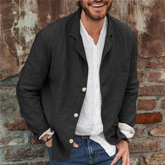 Man wearing a black lightweight cotton linen blazer over a white casual shirt and blue jeans, standing against a rustic brick and weathered wall background.