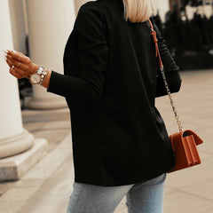 Woman wearing a slim black long-sleeve blazer paired with light blue jeans, accessorized with a watch, bracelets, and a brown crossbody bag.