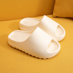 Beige lightweight platform slides made of eco-friendly EVA foam with a thick cushioned sole, designed for comfort and casual wear on soft yellow fabric background.
