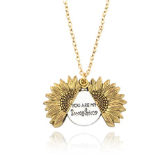Gold sunflower locket necklace with a hidden circular pendant engraved with the phrase "You Are My Sunshine" on a delicate gold chain, reflecting sentimental and personalized jewelry.