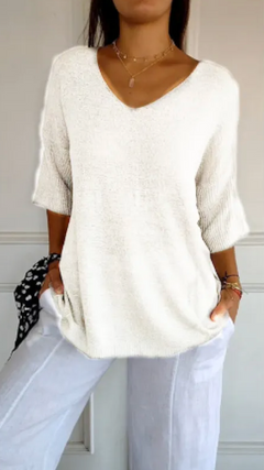 Woman wearing a stretchable, white V-neck knit sweater with three-quarter sleeves paired with white pants, accessorized with delicate layered necklaces and bracelets.