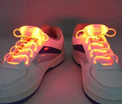 Pair of white sneakers with bright orange LED light-up shoelaces glowing in a dark setting, designed for night visibility and safety.