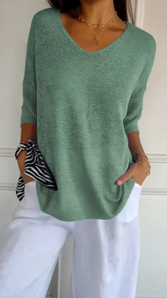 Woman wearing a stretchable green V-neck knit sweater with three-quarter sleeves paired with white pants, accessorized with layered gold necklaces and bracelets.