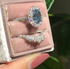 Elegant blue zircon ring with geometric design surrounded by sparkling stones, paired with a matching diamond-accented band, displayed in a velvet ring box.