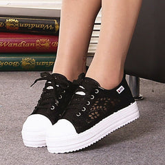 Close-up of women's black canvas sneakers with a chunky white platform sole and lace-up design, featuring subtle floral cutout patterns for breathable, stylish comfort.
