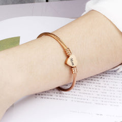 Rose gold textured cable bracelet featuring a heart-shaped charm engraved with "Mom" worn on a wrist, ideal as a personalized Mother's Day gift.