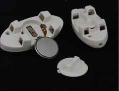 White plastic battery holders with compartments and a small round button cell battery, displayed on a black background.