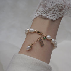 Close-up of a wrist wearing a white natural zircon pearl bracelet with gold accents and delicate charms, styled with a lace cuff and soft fabric background.