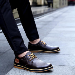 Men's brown genuine leather lace-up casual Oxford shoes with tan accents, worn with black pants on a city sidewalk, stylish and comfortable business footwear.