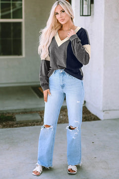 Woman wearing a black and gray colorblock V-neck knit long sleeve top paired with light blue distressed wide-leg jeans and white slide sandals, standing outdoors.