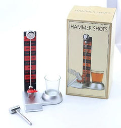 Party drinking game set with a small hammer, shot glass, and a vertical scale for scoring, displayed next to its packaging box.