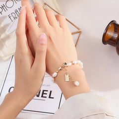 Close-up of a delicate white pearl bracelet with gold accents and a small charm, elegantly worn on a wrist against a softly lit background.
