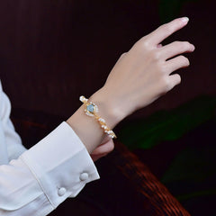Elegant gold-plated bracelet featuring braided wire and natural pearls, worn on a wrist with a white cuffed sleeve, highlighting its vintage-inspired design.