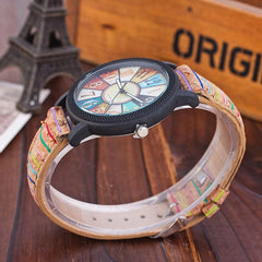 Vintage-inspired women’s quartz wristwatch with a multicolor dial and retro leather strap, styled on a wooden table near a small Eiffel Tower decoration.