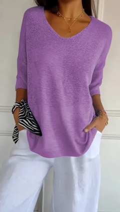 Woman wearing a stretchable lilac V-neck knit sweater paired with white pants and accessorized with layered gold necklaces, bracelets, and a zebra-patterned scarf tied on the wrist.