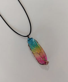 Rainbow aura quartz pendant necklace featuring a handcrafted wire-wrapped tree of life design on a black cord, showcasing vibrant blue, green, yellow, and pink hues.