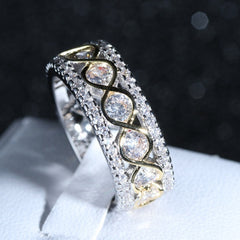 Close-up of a two-tone gold and silver ring with round cut cubic zirconia stones set in a wide, multi-row infinity design on a white display stand against a dark background.