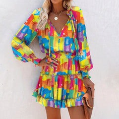Woman wearing a colorful patchwork long sleeve dress with puffed sleeves and tiered ruffle skirt, accessorized with a necklace and holding a brown clutch bag.