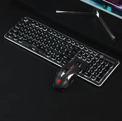 Black USB wired gaming keyboard with backlit keys paired with a matching illuminated gaming mouse on a black surface beneath a monitor stand.