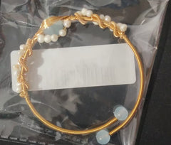 Gold-plated braided wire bracelet featuring white pearls, styled as a vintage cuff with adjustable ends showcasing translucent beads, packaged in clear wrapping.