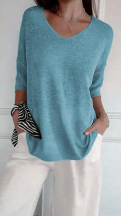 Woman wearing a stretchable blue V-neck knit sweater paired with white pants, accessorized with layered necklaces and a zebra-patterned scarf on her wrist.