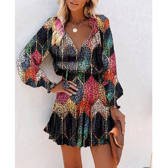 Woman wearing a colorful patchwork long sleeve dress with puff sleeves and a fitted waist, accessorized with layered necklaces and holding a brown clutch.
