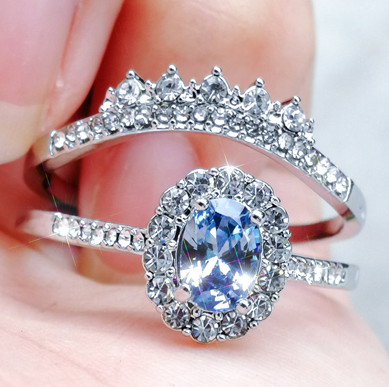 Close-up of a geometric-patterned silver ring featuring an oval blue zircon center stone surrounded by smaller clear gemstones, styled as a delicate and elegant accessory.