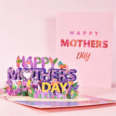 Colorful 3D pop-up floral bouquet card with "Happy Mothers Day" message, featuring purple flowers and small decorative birds, placed in front of a matching pastel greeting card.