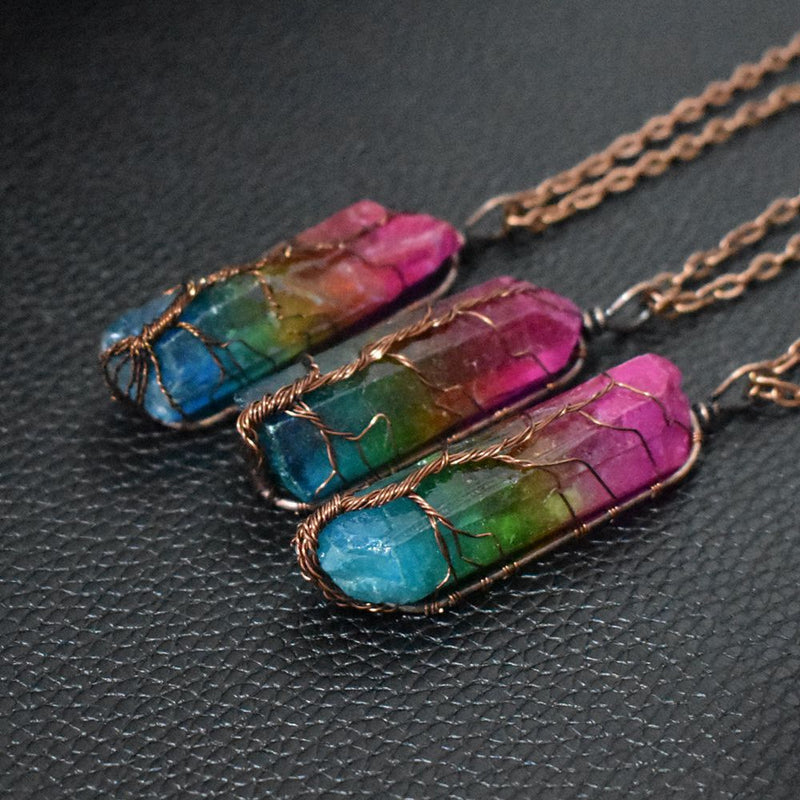 Three handcrafted crystal pendant necklaces featuring rainbow-colored quartz wrapped in copper wire, displayed on a textured black surface.