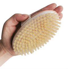 Hand holding a natural bristle bath brush with an oval wooden base and a fabric strap for easy grip, designed for exfoliating and skin care.