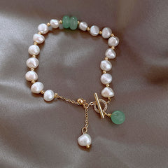 Delicate adjustable bracelet featuring irregular white freshwater pearls, natural green jade beads, and gold-tone accents, elegantly displayed on a soft fabric background.