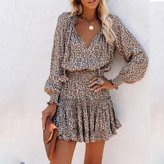 Woman wearing a leopard print long sleeve dress with puff sleeves and a cinched waist, accessorized with layered necklaces and holding a brown clutch.