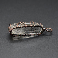 Clear crystal pendant wrapped in intricate copper wire, featuring a tree of life design, set against a dark background highlighting handcrafted boho jewelry style.
