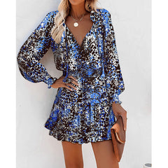 Woman wearing a blue and black floral print long sleeve dress with puff sleeves and a fitted waist, accessorized with a necklace and holding a brown clutch purse.