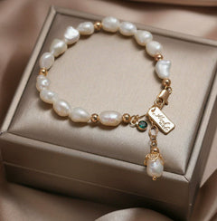 Elegant white pearl bracelet with natural zircon and gold accents, featuring a personalized charm, displayed on a luxurious beige fabric background.