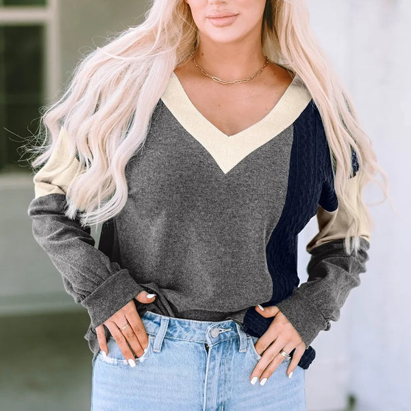 Woman wearing a stylish long sleeve knit top with a black, gray, cream, and navy colorblock design paired with light blue jeans, showcasing a casual yet chic look.