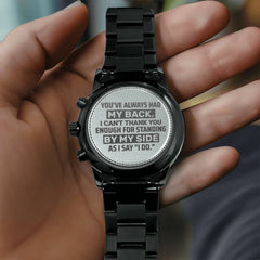 Hand holding a black engraved men's chronograph watch with a heartfelt message on the caseback, celebrating support and friendship for a special occasion gift.