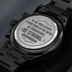 Close-up of the back of a black chronograph watch with an engraved inspirational scripture from 1 Corinthians 16:13 encouraging strength and courage in faith.