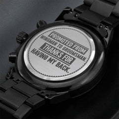 Close-up of the back of a men's black chronograph wristwatch with an engraved message appreciating a groomsman, featuring a stainless steel case and black metal band.