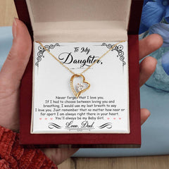 Hand holding open red velvet jewelry box displaying a gold heart-shaped necklace with a sparkling crystal on a card featuring a heartfelt message from a father to his daughter.