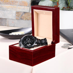 Men’s black chronograph watch with a sleek metal band displayed in an elegant polished wooden gift box, suitable as a faith-inspired, engraved gift.