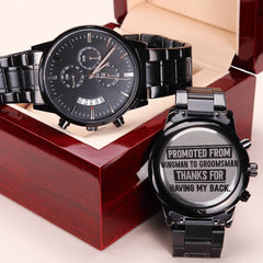 Black chronograph men's watch with metal link band displayed on and beside a polished wooden gift box, featuring engraved backplate message honoring a groomsman promotion.