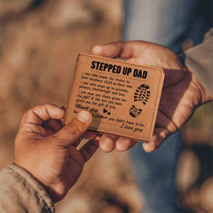 Two hands exchanging a brown leather bifold wallet embossed with a heartfelt message for a stepdad, featuring footprints and a sincere thank you note.